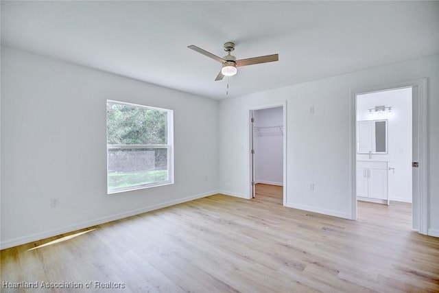 unfurnished bedroom featuring a walk in closet, ensuite bathroom, light hardwood / wood-style flooring, and ceiling fan