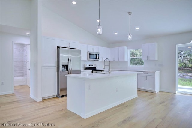 kitchen with white cabinets, pendant lighting, stainless steel appliances, and an island with sink