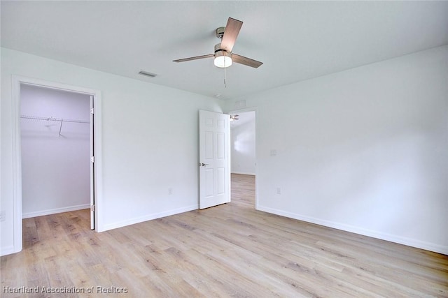 unfurnished bedroom featuring ceiling fan, light hardwood / wood-style floors, a spacious closet, and a closet