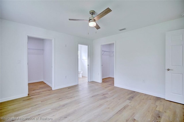 unfurnished bedroom with light wood-type flooring, ensuite bathroom, a spacious closet, and ceiling fan