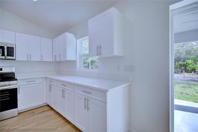 kitchen with white cabinets, light hardwood / wood-style floors, lofted ceiling, and range