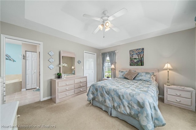 bedroom featuring light carpet, ceiling fan, ensuite bathroom, a tray ceiling, and a closet