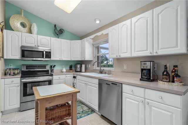 kitchen featuring vaulted ceiling, light tile patterned floors, sink, white cabinets, and stainless steel appliances