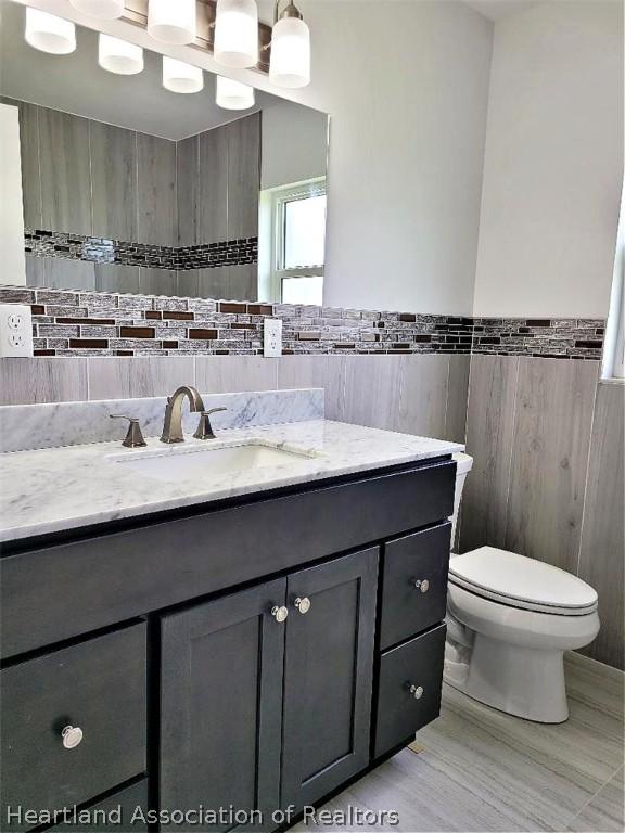 bathroom featuring vanity, toilet, and tile walls