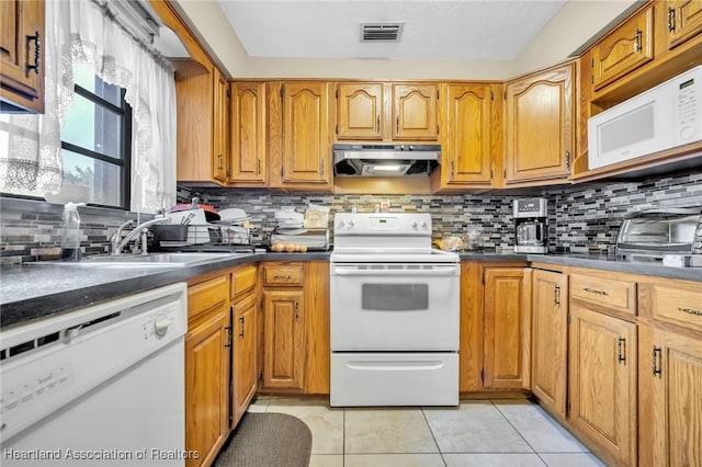 kitchen featuring light tile patterned floors, dark countertops, visible vents, white appliances, and under cabinet range hood