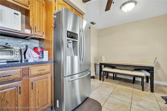 kitchen with stainless steel fridge, tasteful backsplash, dark countertops, white microwave, and light tile patterned flooring