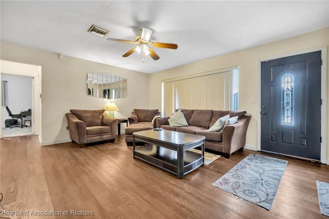 living room with a ceiling fan, visible vents, baseboards, and wood finished floors