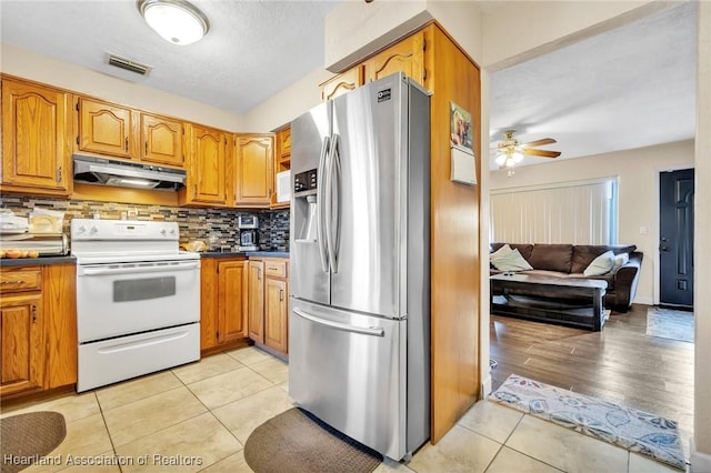 kitchen featuring light tile patterned floors, under cabinet range hood, electric range, visible vents, and stainless steel fridge with ice dispenser