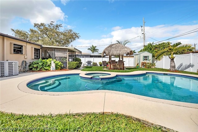 view of pool featuring a fenced backyard, a pool with connected hot tub, cooling unit, and an outdoor structure