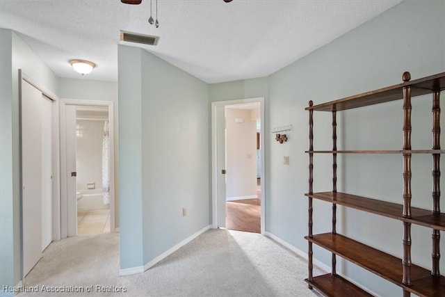 hall with visible vents, a textured ceiling, baseboards, and carpet