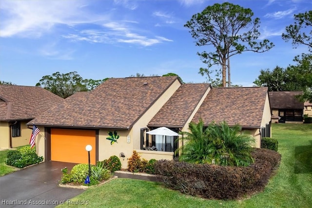 view of front facade featuring aphalt driveway, a front yard, roof with shingles, stucco siding, and a garage