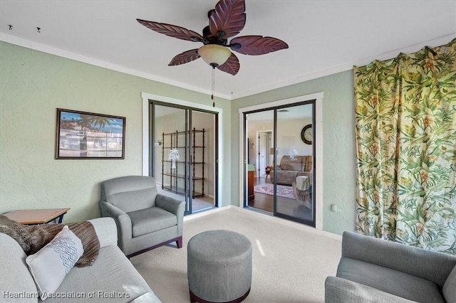 living area with baseboards, ornamental molding, ceiling fan, carpet flooring, and a textured wall