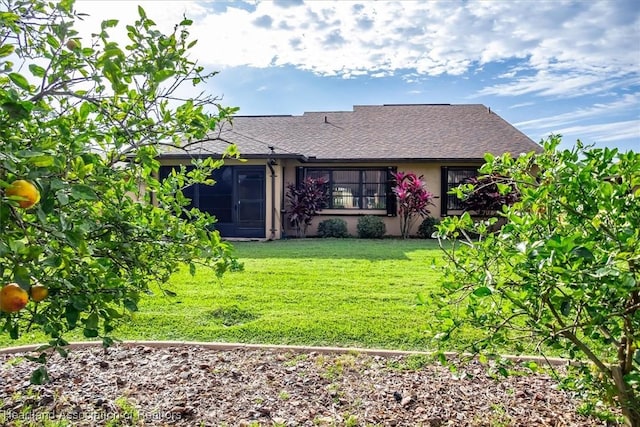 rear view of property with stucco siding, a lawn, and roof with shingles