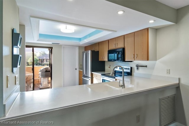 kitchen with a peninsula, a tray ceiling, recessed lighting, stainless steel appliances, and light countertops