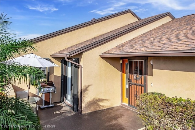 view of exterior entry featuring stucco siding and a shingled roof