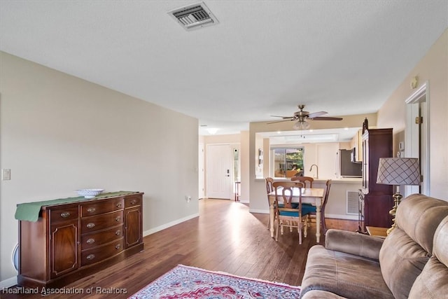 living room with visible vents, a ceiling fan, baseboards, and dark wood-style flooring