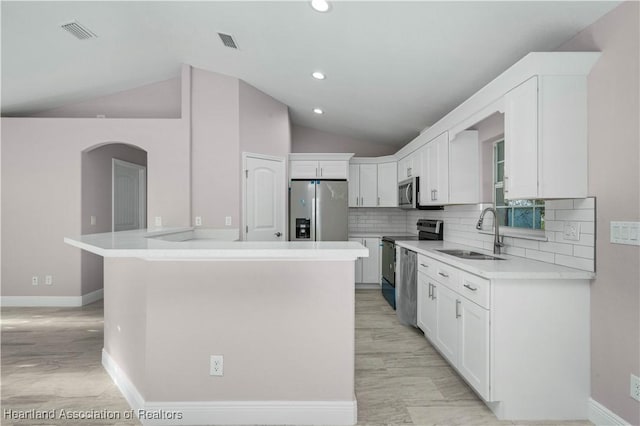 kitchen with sink, appliances with stainless steel finishes, white cabinetry, a kitchen island, and vaulted ceiling