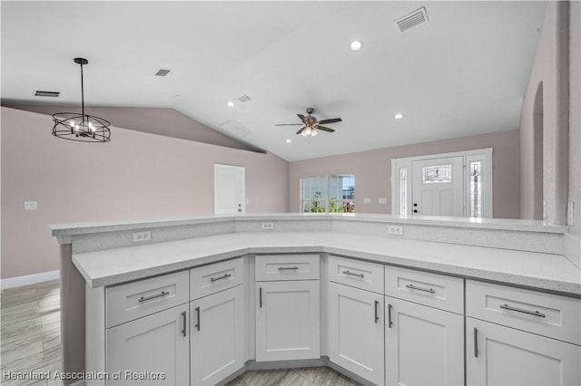 kitchen featuring ceiling fan with notable chandelier, decorative light fixtures, lofted ceiling, white cabinets, and light stone counters