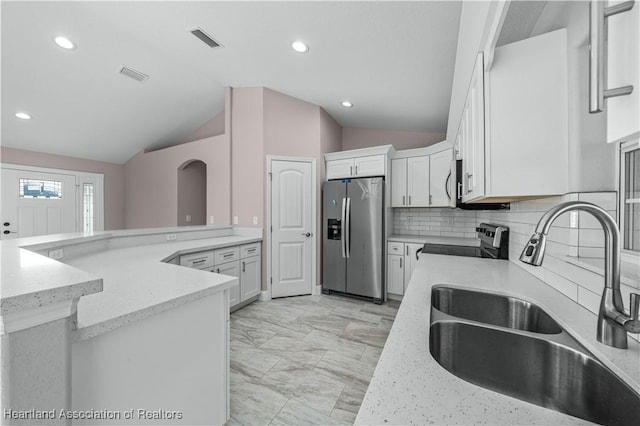 kitchen featuring sink, appliances with stainless steel finishes, white cabinetry, light stone counters, and vaulted ceiling