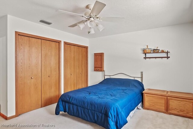 bedroom featuring multiple closets, ceiling fan, and light colored carpet