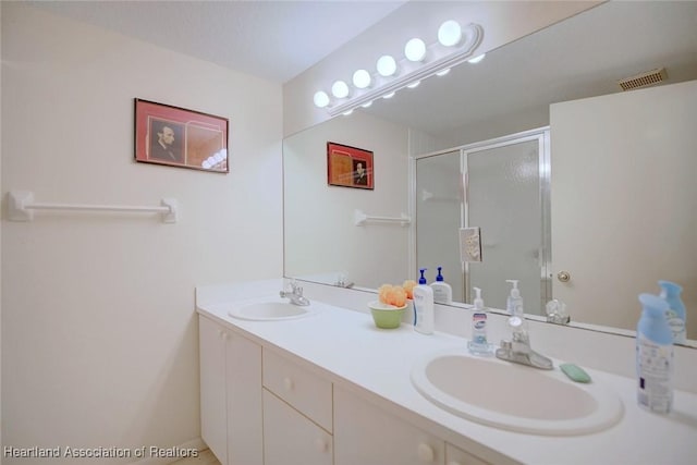 bathroom with double vanity, visible vents, a sink, and a shower with shower door