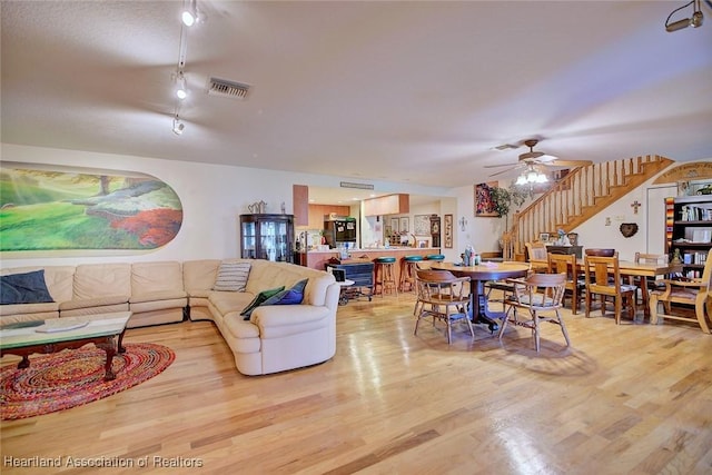 living area featuring a ceiling fan, visible vents, light wood finished floors, and stairs