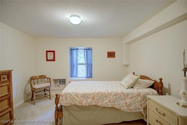 bedroom featuring light carpet, a textured ceiling, and an AC wall unit