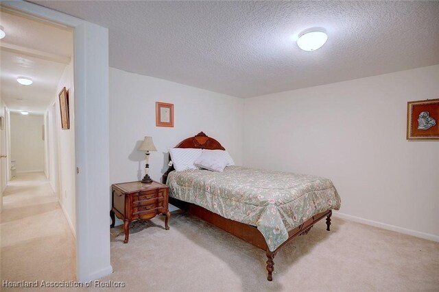 bedroom with light carpet, a textured ceiling, and baseboards