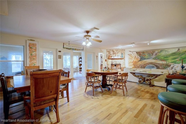 dining space with a stone fireplace, light wood-type flooring, visible vents, and a ceiling fan