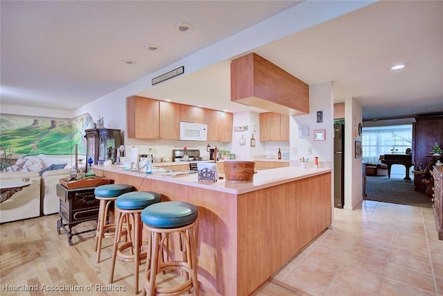 kitchen featuring white microwave, refrigerator, a peninsula, light countertops, and gas stove