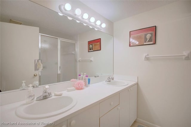 full bathroom with a stall shower, a sink, baseboards, and double vanity