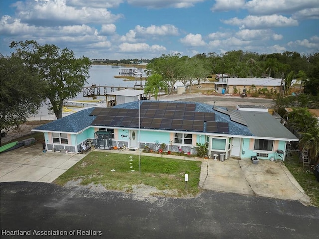 view of front of property featuring solar panels, driveway, a water view, and a front yard