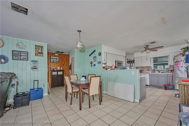 dining area with ceiling fan, wood walls, visible vents, and light tile patterned floors
