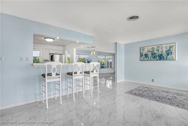 115 Elwa Pl, West Palm Beach, FL 33405 - kitchen with freestanding refrigerator, a kitchen breakfast bar, light marble finish floors, light countertops, and healthy amount of natural light