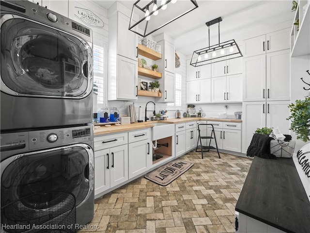 washroom with stacked washer / drying machine, sink, and cabinets