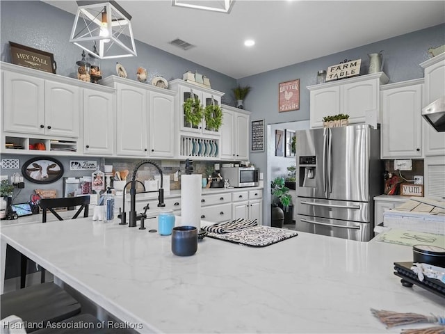 kitchen with a kitchen bar, pendant lighting, stainless steel appliances, and white cabinetry