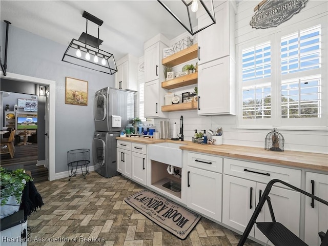 kitchen featuring white cabinetry, wooden counters, tasteful backsplash, decorative light fixtures, and stacked washer / dryer