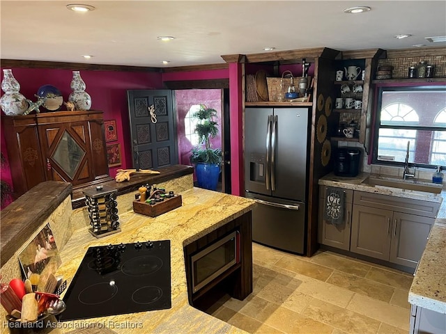 kitchen with stainless steel refrigerator with ice dispenser, black electric stovetop, sink, light stone counters, and crown molding