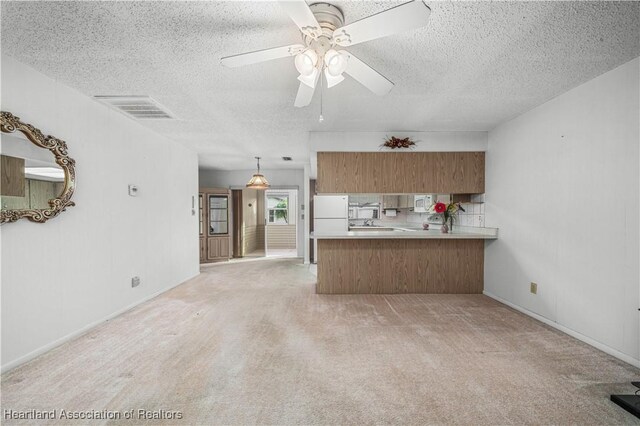 170 Parkview Cir, Lake Placid, FL 33852 - kitchen featuring brown cabinets, a textured ceiling, a peninsula, white appliances, and light colored carpet