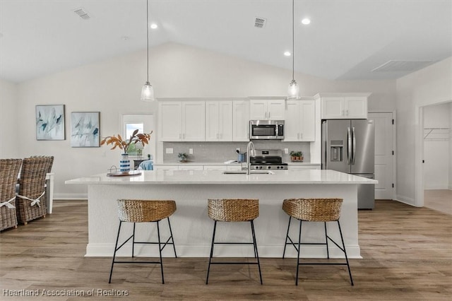 4954 San Ignacio Dr, Sebring, FL 33872 - kitchen featuring appliances with stainless steel finishes, a center island with sink, white cabinetry, light wood-style flooring, and high vaulted ceiling