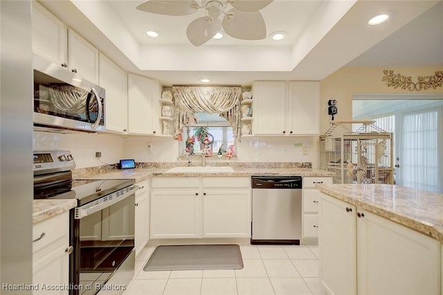 kitchen with white cabinets, sink, ceiling fan, a tray ceiling, and stainless steel appliances