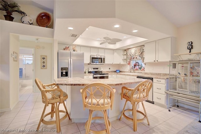 kitchen with a raised ceiling, white cabinetry, a center island, and appliances with stainless steel finishes