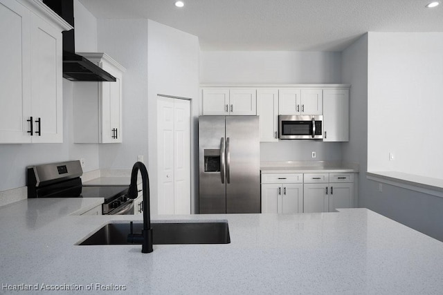 kitchen featuring white cabinetry, sink, appliances with stainless steel finishes, and wall chimney range hood