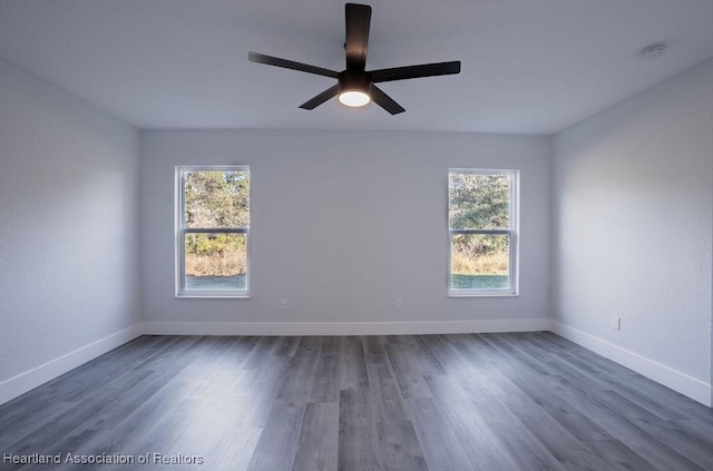 empty room with ceiling fan, a healthy amount of sunlight, and dark hardwood / wood-style flooring