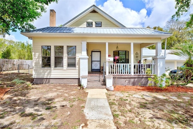 bungalow-style home featuring fence, metal roof, a porch, and a chimney