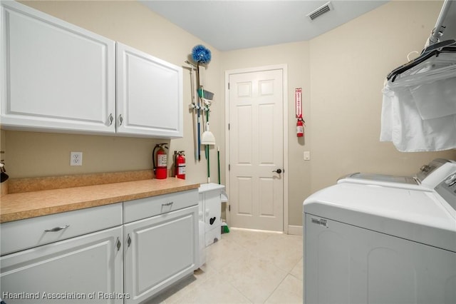 clothes washing area featuring cabinets, washing machine and dryer, and light tile patterned floors