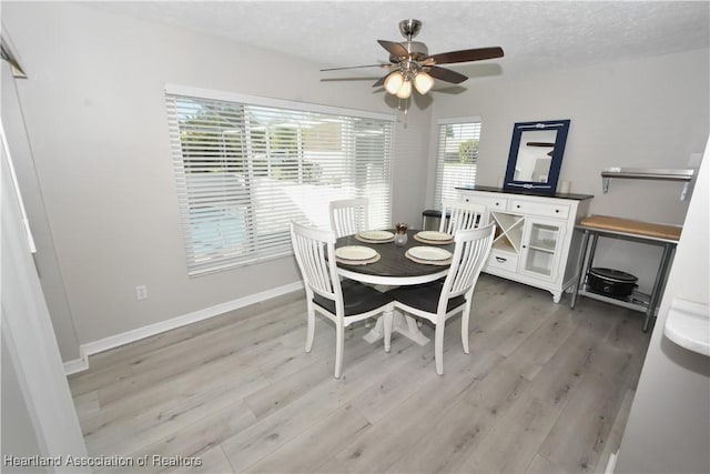 dining area with baseboards, a textured ceiling, light wood-style flooring, and a ceiling fan