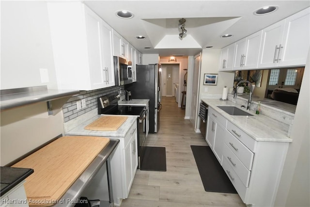 kitchen featuring light wood-type flooring, a sink, white cabinetry, stainless steel appliances, and decorative backsplash