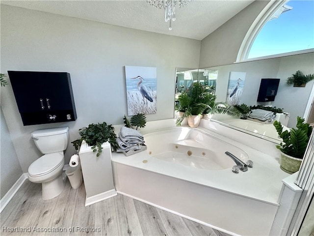 bathroom with toilet, a textured ceiling, a jetted tub, wood finished floors, and baseboards