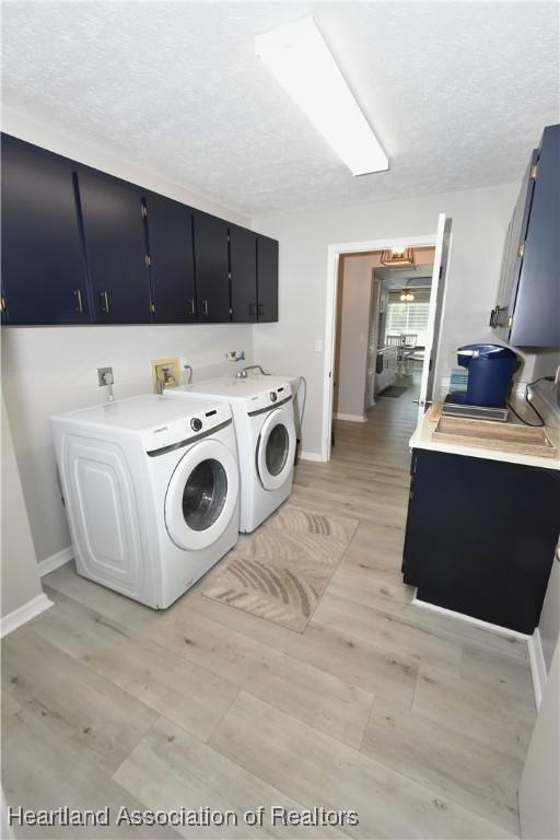 laundry room featuring baseboards, light wood-style floors, cabinet space, a textured ceiling, and independent washer and dryer